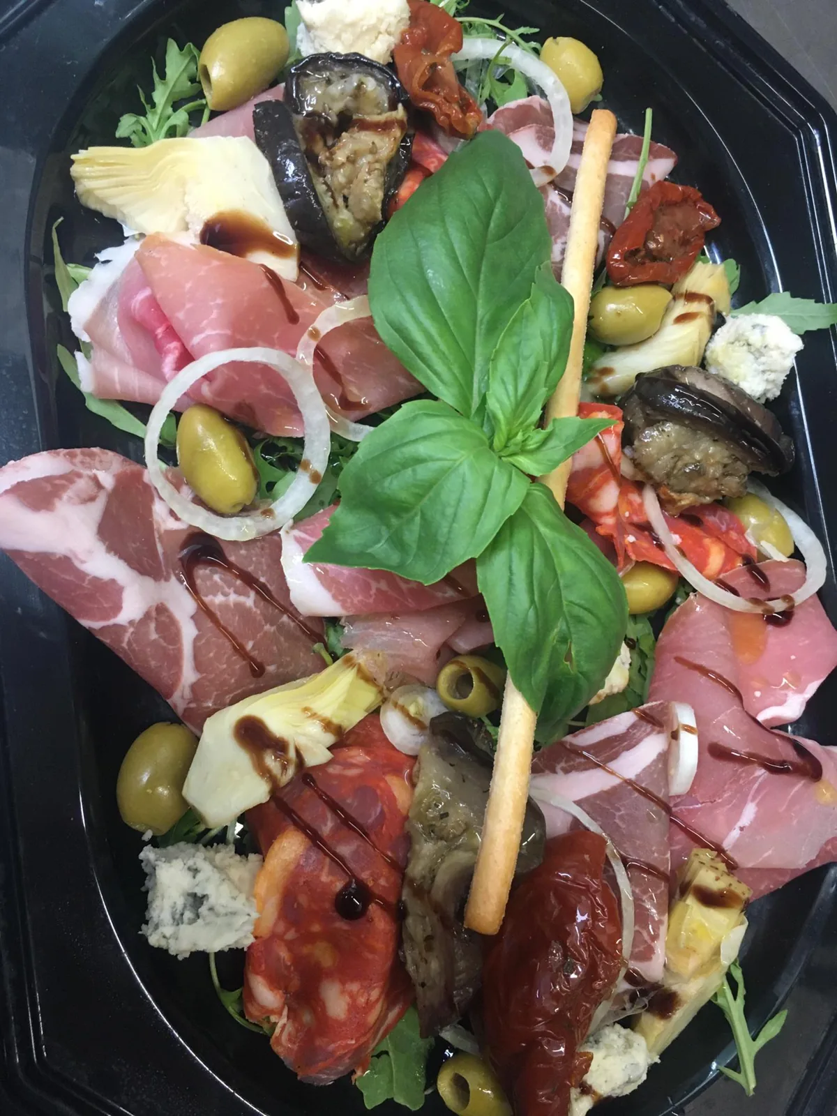 Assiette d'antipasti avec charcuterie italienne, olives, artichauts et basilic