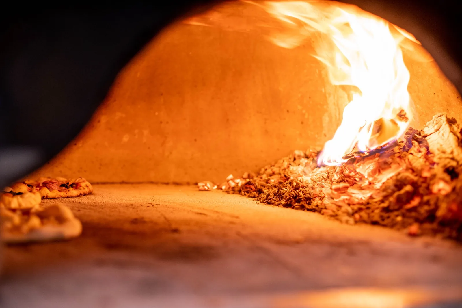 Flammes dans le four à bois, pizzas en cuisson